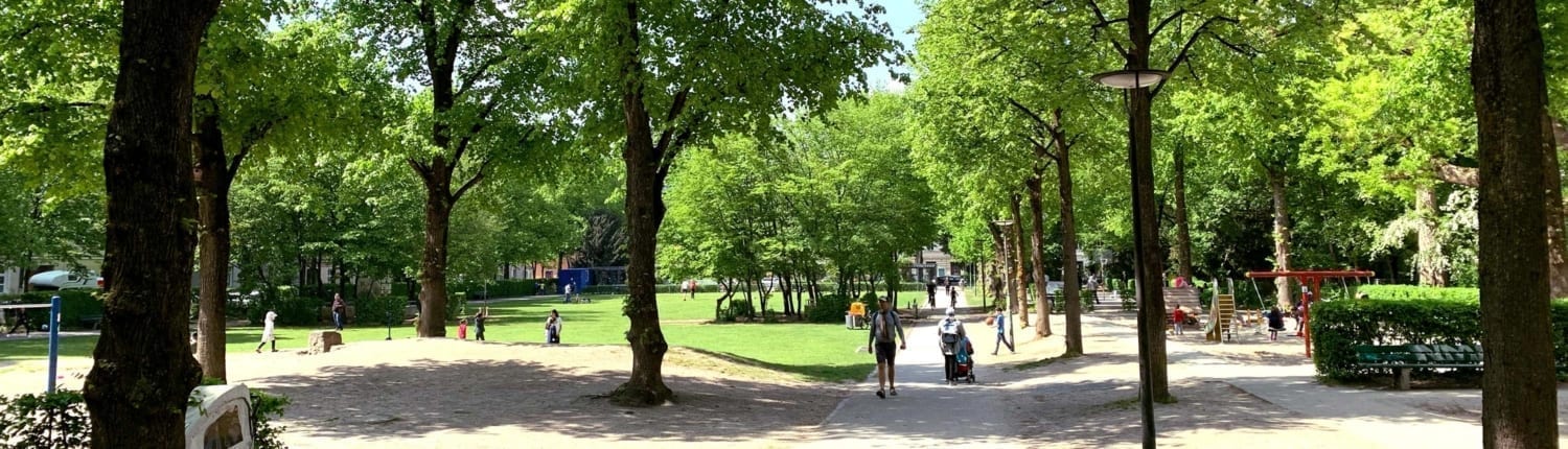 Blick auf den Piusplatz bei Tag. Park mit Spielplatz und Menschen.